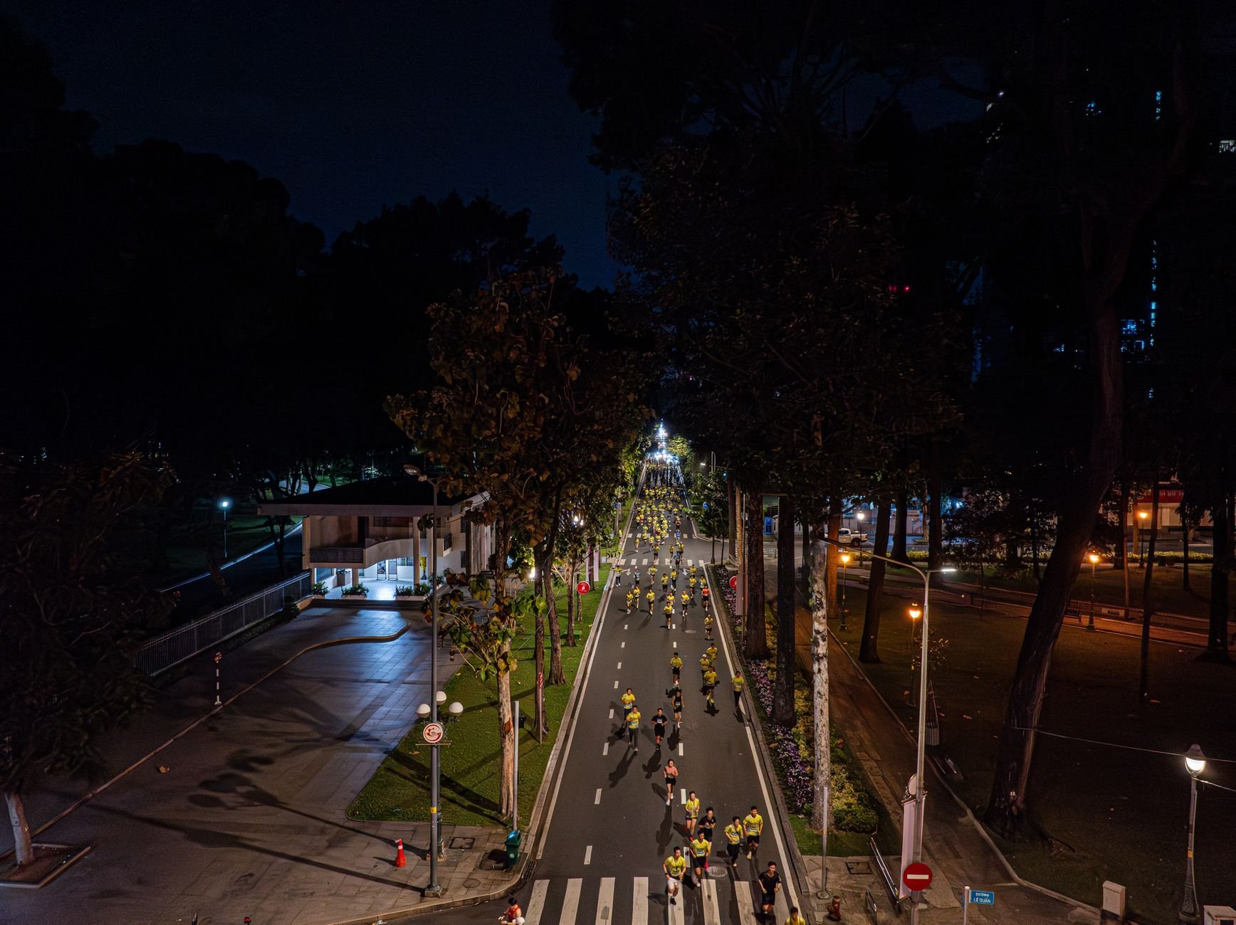 Aerial view of a nighttime marathon on a lit urban street lined with trees