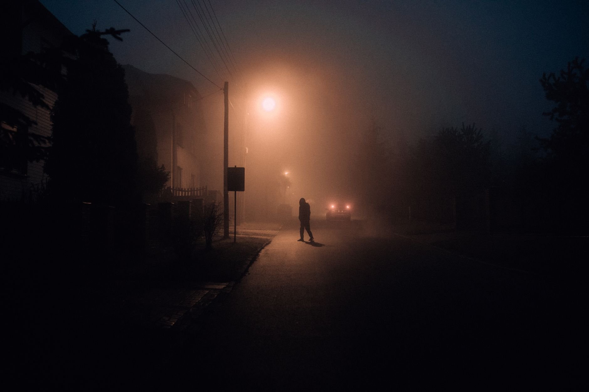 A lone silhouette walking down a foggy street at night with street lamps casting a moody glow